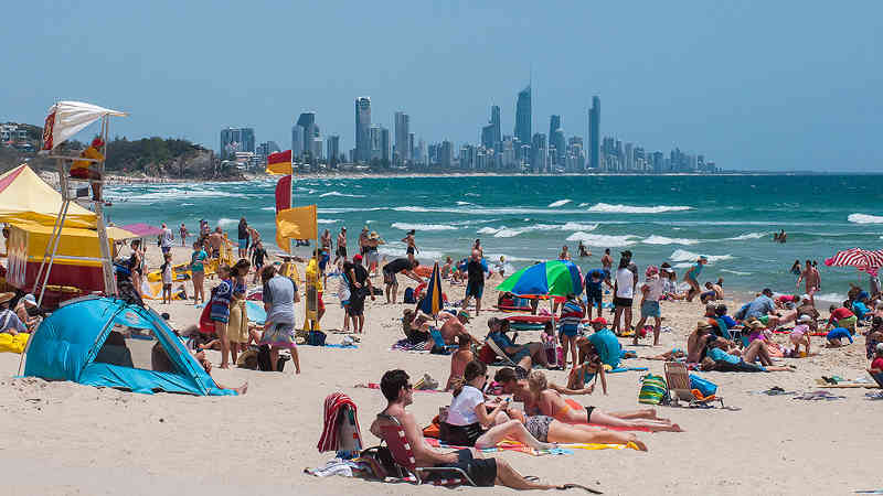 Queensland and visitors enjoying the sun and surf on a beach at Burleigh Heads on the Gold Coast with view of the Gold Coast Skyline in the background